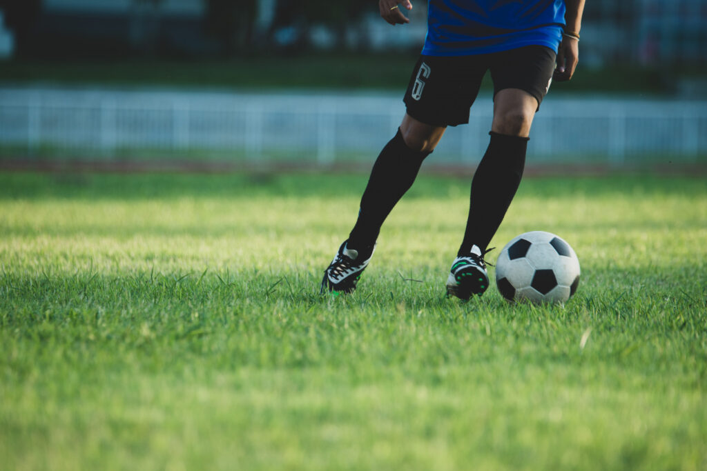 Por que as categorias de base viraram o melhor investimento do futebol Homem com camisa azul e calças pretas chutando uma bola de futebol em campo.