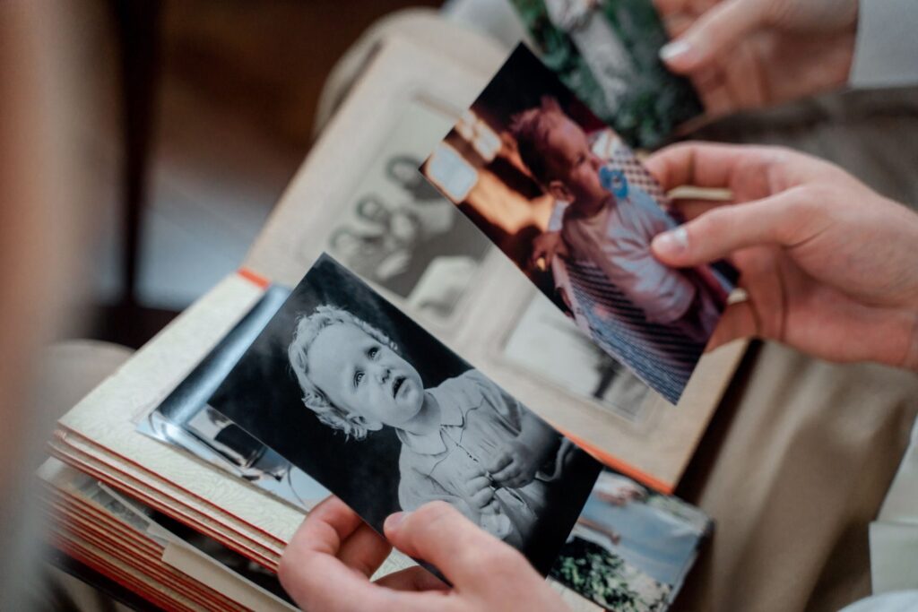Mãos folheando um álbum antigo e segurando duas fotografias de família, uma em preto e branco e outra colorida