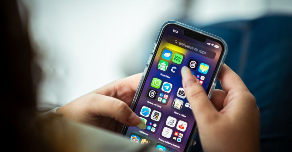 Mão segurando smartphone com vários ícones de aplicativos na tela.
