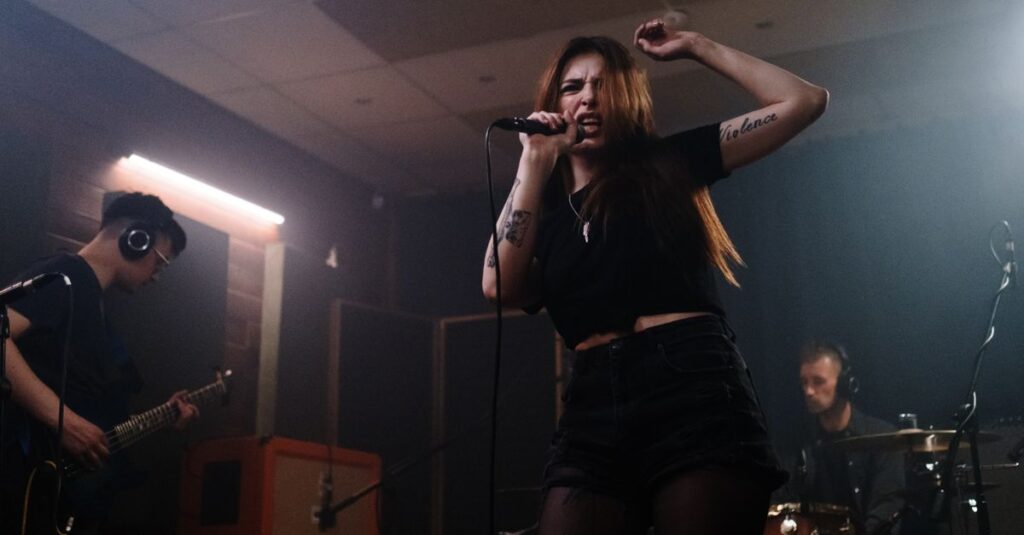 Cantora em destaque no palco, cantando em um estúdio com músicos ao fundo.
